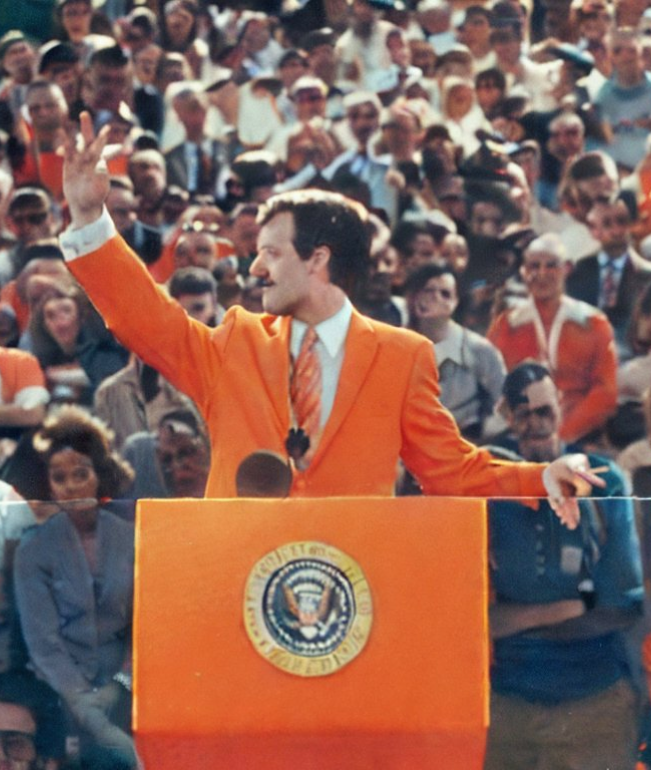 Mayor in orange suit addressing a crowd